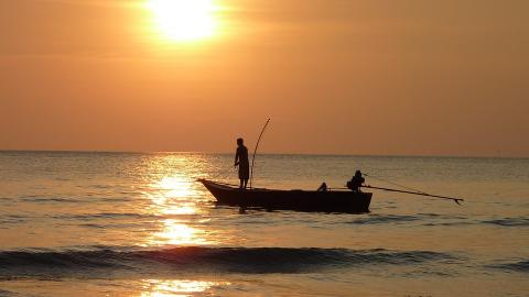 Man fishing in boat at sunset