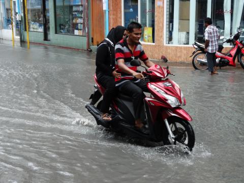 Two people on a motor bike in a flood after rain